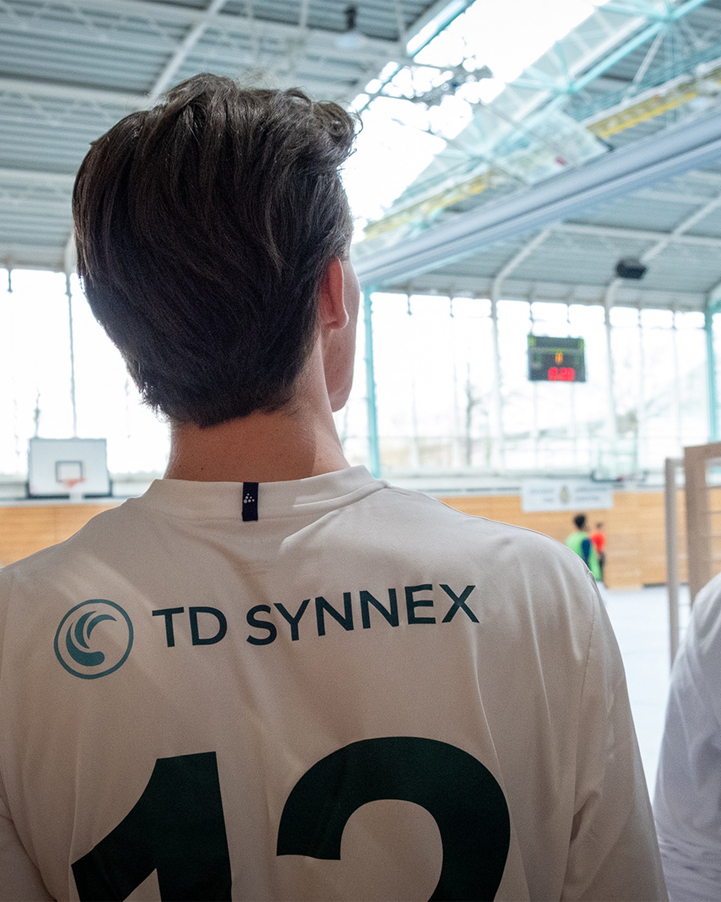 Fußballspieler in weißen TD-SYNNEX-Trikots von hinten in einer Sporthalle