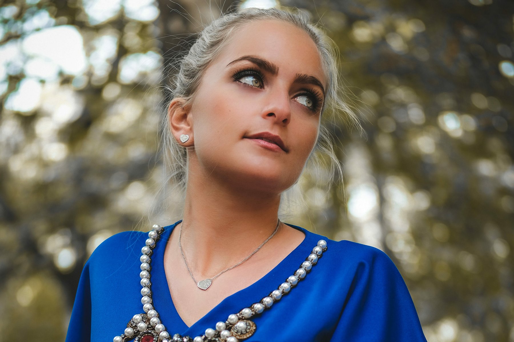 Frau in blauem Kleid mit Perlenkette, Portrait im Wald bei natürlichem Licht