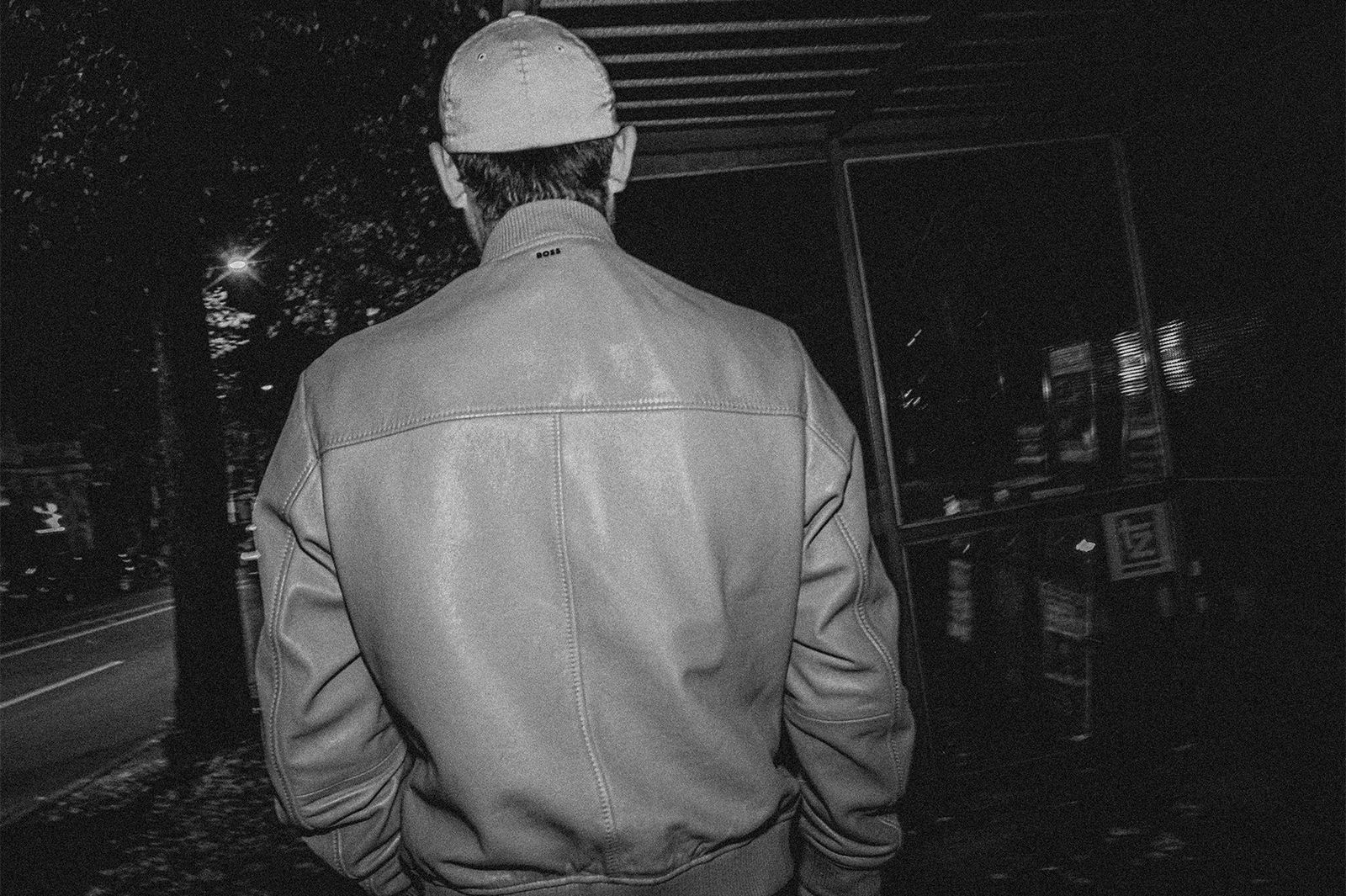Schwarzweiß-Aufnahme eines Mannes mit Cap von hinten bei Nacht