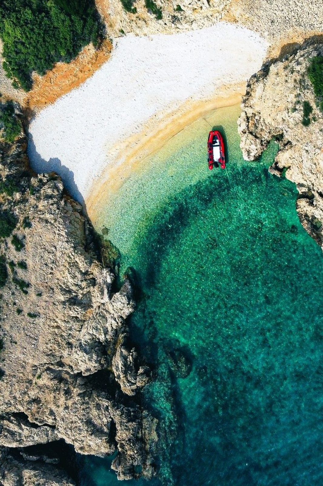 Drohnenaufnahme einer türkisblauen Bucht mit rotem Boot für Macan Reisen HR
